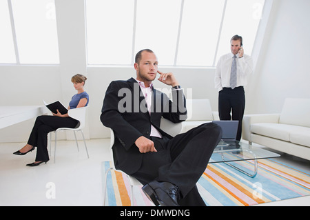 Drei Geschäftsleute in einem Büro eines auf ein Telefon arbeitet auf einem digitalen Tisch und sitzen auf einem Stuhl. Stockfoto