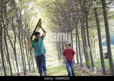 Ein Mann mit einem Solar-Panel, eine Allee von Bäumen, die Begleitung eines Kindes. Stockfoto