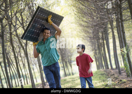 Ein Mann mit einem Solar-Panel, eine Allee von Bäumen, die Begleitung eines Kindes. Stockfoto