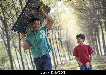 Ein Mann mit einem Solar-Panel, eine Allee von Bäumen, die Begleitung eines Kindes. Stockfoto