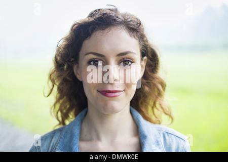 Eine junge Frau in einer ländlichen Landschaft mit vom Wind verwehten lockiges Haar Lächeln auf den Lippen. Stockfoto