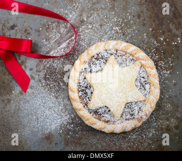 Hausgemachte Zuckerglasur bestäubt Mince Pie auf eine rustikale graue Metalloberfläche mit rotem Band Stockfoto