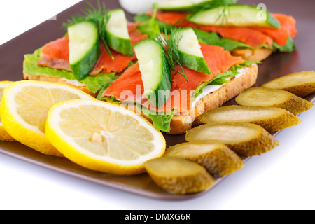 Lachs Sandwiches mit Salat, frische und eingelegte Gurken, Zwiebel, Zitrone auf Platte isoliert auf weißem Hintergrund. Stockfoto