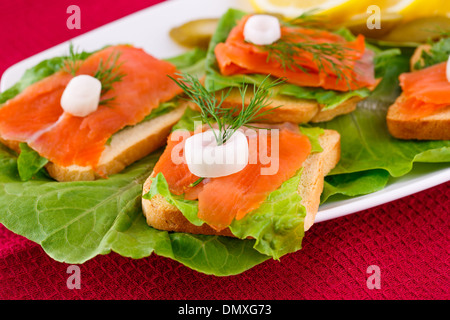 Lachs Sandwiches mit Salat, frische und eingelegte Gurken, Zwiebel, Zitrone auf Platte. Stockfoto