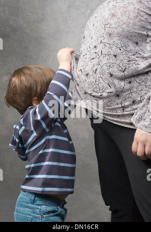 Kleiner Junge unter seiner schwangeren Mutter Bluse gucken Stockfoto