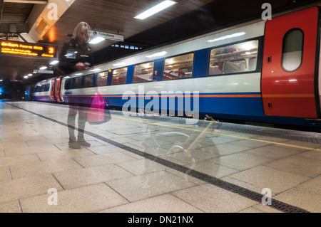 Geisterhafte Figur einer Frau, die auf dem Bahnsteig am Bahnhof Leicester wartet, mit einem East Midlands-Zug im Hintergrund Stockfoto