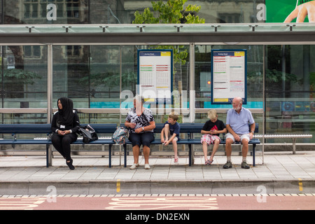 Menschen sitzen und warten auf Bus Bushaltestelle Tierheim, Bristol, UK Stockfoto