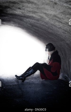 eine Frau in einem roten Mantel sitzt in einem dunklen tunnel Stockfoto