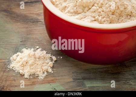 Gluten freie Kokosmehl in einer Schüssel rote Steinzeug und verschüttete auf einem Holzbrett Stockfoto