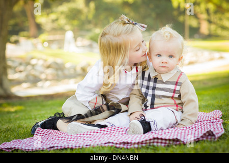 Süßes kleines Mädchen küsst ihr Baby Bruder auf seiner Wange im Freien im Park. Stockfoto