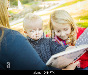 Mutter ein Buch zu lesen, um ihre zwei entzückende Blonde Kinder Winterjacken im Freien tragen. Stockfoto