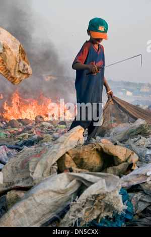 Ein Kind Arbeiter junge arbeitet in der Nähe von brennenden Haufen Müll auf der verschmutzten Stung Meanchey Deponie in Phnom Penh, Kambodscha. Stockfoto