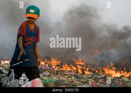 Ein Kind Arbeiter junge arbeitet in der Nähe von brennenden Haufen Müll auf der verschmutzten Stung Meanchey Deponie in Phnom Penh, Kambodscha. Stockfoto