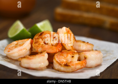 Frische gebratene Garnelen mit Limettenscheiben auf Butterbrotpapier mit Toast Brotscheiben hinten Stockfoto