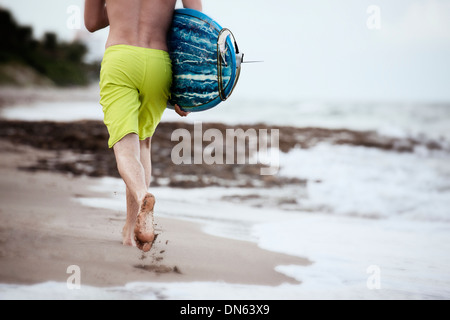 Hispanic Mann mit Surfbrett am Strand Stockfoto