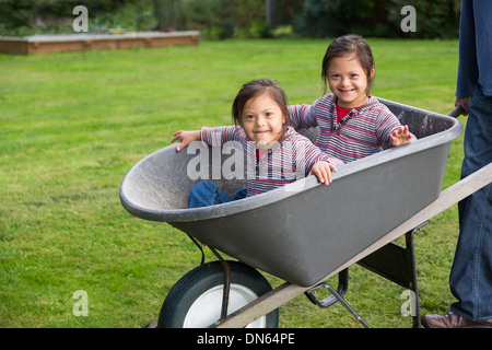 Zwillinge mit Down-Syndrom lächelnd in Schubkarre Stockfoto