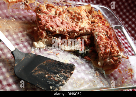 Ein Stück hausgemachte Fleisch Lasagne auf einem weißen Teller mit einer Flasche Rotwein im Hintergrund auf einer karierten Tischdecke Stockfoto