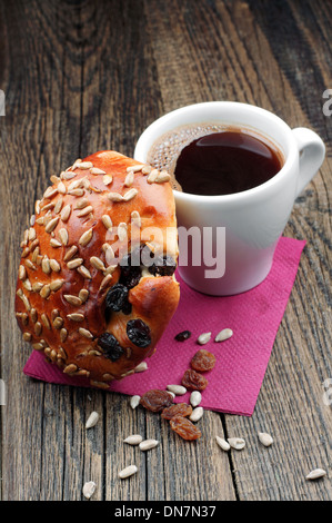 Tasse Kaffee und Brötchen mit Sonnenblumenkernen und Rosinen auf Holztisch Stockfoto