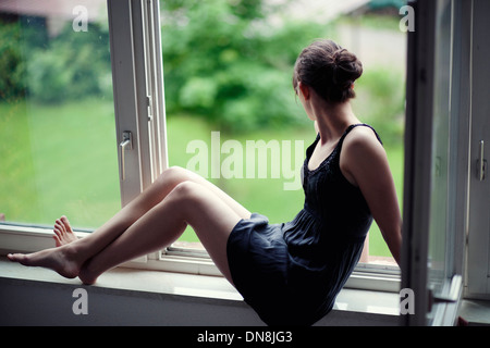 Junge Frau sitzt auf einem Fensterbrett Stockfoto