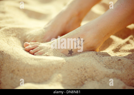 Füße mit Tatoo am Sandstrand Stockfoto