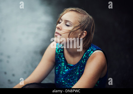 Junge Frau sitzt im Regen auf der Straße Stockfoto