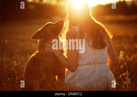 Frau mit Hund sitzt auf einer Wiese bei Sonnenuntergang Stockfoto