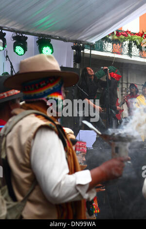 La Paz, Bolivien. 20. Dezember 2013. Aymara-Schamanen (eine typische wollene Mütze mit Ohrenklappen tragen ein Chullo genannt / Chullu unter einen Sombrero) durchführen von Zeremonien zu segnen und feiern den Start der erste Kommunikationssatellit Boliviens während der bolivianischen heavy-Rock-Band Armadura im Hintergrund auf einer Veranstaltung in Plaza Murillo spielt. Tupac Katari Satelliten (benannt nach einer indigenen Held, einen Aufstand gegen die Spanier führte) wurde zu einem Preis von rund $300million gebaut. Bildnachweis: James Brunker / Alamy Live News Stockfoto
