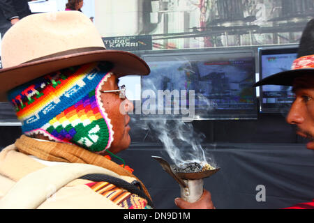 La Paz, Bolivien. 20. Dezember 2013. Aymara-Schamanen (eine typische wollene Mütze mit Ohrenklappen tragen ein Chullo genannt / Chullu unter einen Sombrero) durchführen von Zeremonien zu segnen und feiern den Start der ersten Kommunikationssatelliten Boliviens auf einer Veranstaltung in Plaza Murillo. Der Start wird live auf einer Großleinwand von der Raumstation XiChang in China im Hintergrund übertragen. Tupac Katari Satelliten (benannt nach einer indigenen Held, einen Aufstand gegen die Spanier führte) wurde zu einem Preis von rund $300million gebaut. Bildnachweis: James Brunker / Alamy Live News Stockfoto