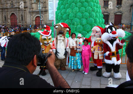 La Paz, Bolivien. 21. Dezember 2013.  Ein Aymara Familie Pose für Sofortbilder mit Santa und beliebten Film / Comic-Figuren im Plaza San Francisco. Im Hintergrund ist eine ökologische Weihnachtsbaum von recyceltem Kunststoff-Getränkeflaschen hergestellt. Der Baum ist mehr als 15m hoch und enthält ca. 50.000 Flaschen. Bildnachweis: James Brunker / Alamy Live News Stockfoto