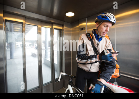 Männliche Radfahrer mit Kuriertasche mit Handy In einem Aufzug Stockfoto