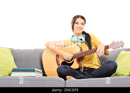 Schöne weibliche Musiker auf Sofa sitzen und eine akustische Gitarre zu spielen Stockfoto