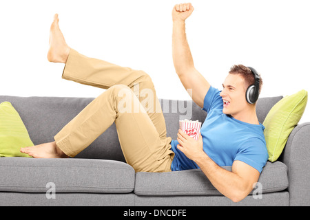 Aufgeregt Kerl auf eine moderne Couch liegen und Musik hören Stockfoto