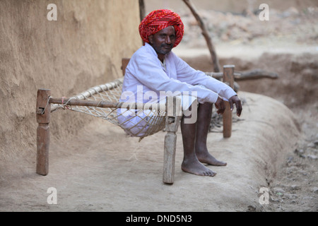 Tribal Mann sitzt auf einem Feldbett außerhalb seines Hauses, Madhya Pradesh, Indien. Bhil Stamm. Stockfoto