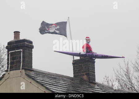 Tideswell, Derbyshire, UK.  23. Dezember 2013.  Santa sitzt in einem Kanu, genannt "HMS Tidza" auf dem Dach des The Anchor Inn, einer Gastwirtschaft 15. Jahrhundert als strömendem Regen und starkem Wind fegen über den Peak District.  Tideswell ist von den lokalen Bewohnern liebevoll als Tidza bezeichnet. Bildnachweis: Deborah Vernon/Alamy Live-Nachrichten Stockfoto