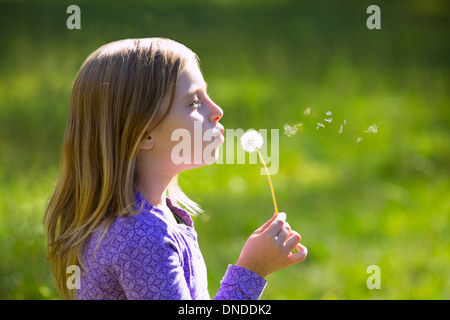 Blonde junge Mädchen bläst Blume Löwenzahn in der grünen Wiese im freien Profilansicht Stockfoto