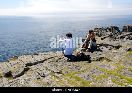 Zwei Frauen Touristen sitzen am Rand der Klippe am Dun Aengus Stone Fort, Aran Islands, Irland. Stockfoto