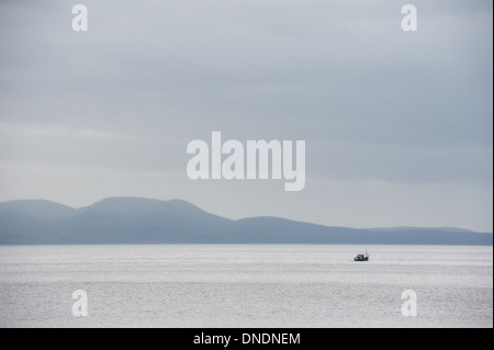 Einsames Fischerboot auf See mit den Bergen im Hintergrund Stockfoto