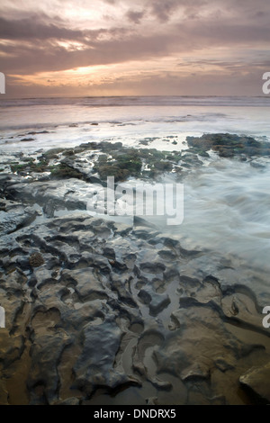 Felsformationen im Dunraven Bay, South Wales, entstehen durch die Kraft des Meeres. Die Sonne untergeht, während die Flut kommt. Stockfoto