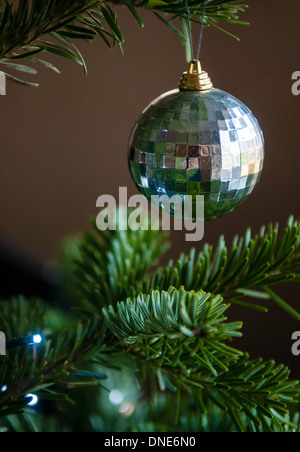 Einzelne Silber gemustert Weihnachtskugel von echten Baum mit Lichterketten hängen. Stockfoto