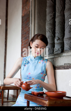Junge Frau trägt Cheongsam und Betrieb Teekanne Stockfoto