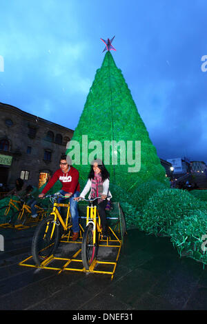 La Paz, Bolivien. 24. Dezember 2013. Einheimischen Pedal auf Fahrrädern verbunden, Batterien, elektrischen Energie für die Beleuchtung auf eine ökologische Weihnachtsbaum im Plaza San Francisco bieten. Der Baum ist mehr als 15m hoch, enthält ca. 50.000 recycelten Kunststoff-Getränkeflaschen und war ein Projekt konzipiert und geplant von der Stadtverwaltung von La Paz. Bildnachweis: James Brunker / Alamy Live News Stockfoto