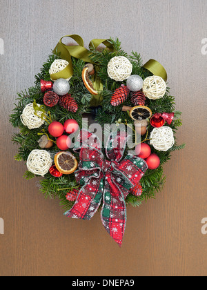 Adventskranz mit Dekorationen und Schleife an der Holztür angebracht Stockfoto