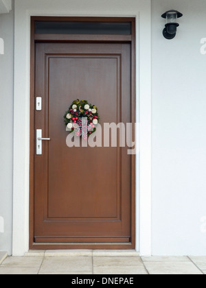 Adventskranz mit Dekorationen und Schleife an der Holztür angebracht Stockfoto