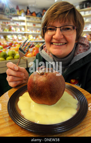 Beate Luehs vom Herzapfelhof (Herz Apple Farm) sitzt hinter einer Platte mit einem Bratapfel Boskop im Hofladen in der Region Altes Land in Jork, Deutschland, 18. Dezember 2013. Foto: Ingo Wagner/dpa Stockfoto