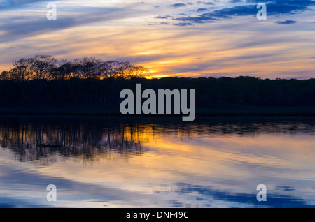 Die Sonne geht über Marschland im späten Frühjahr in Niantic East Lyme Connecticut Vereinigte Staaten Mai 2013. Aufgenommen während der blauen Stunde bei Sonnenuntergang gibt es Streifen von Gold-Gelb in der dunkel lila, blauer Himmel mit Cirruswolken im Wasser der Salzwasser Moor Marschland Backwaters mit einer Insel spiegeln, und Bäume in der Silhouette Silhouette gegen den dramatischen Himmel. Ein schön New England landschaftlich Skyscape Seelandschaft mit Textfreiraum. Stockfoto