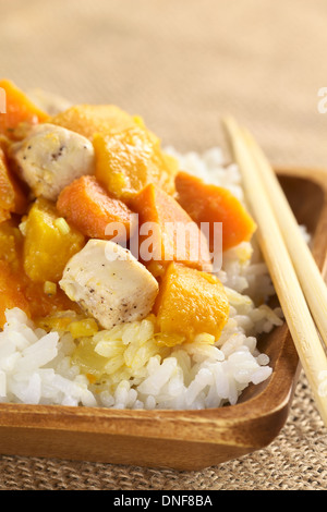 Huhn, Kürbis und Süßkartoffeln Curry serviert auf Reis in Holzplatte mit Stäbchen Stockfoto