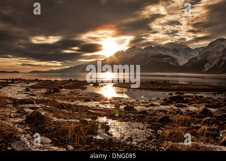 Eis und Schnee am Strand des Chilkat Inlet in Southeast Alaska als die Sonne untergeht durch Gewitterwolken. Stockfoto