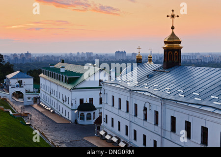 Ukraine Kiew Pechers Lavra internen Gebäude mit Kuppeln und Kreuz bei Sonnenaufgang gegen entfernte moderne Stadtgebäude Stockfoto