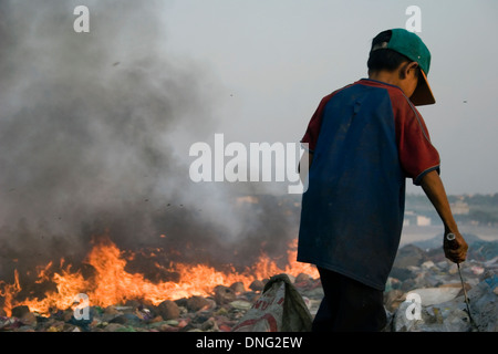 Ein junges Kind Arbeiter junge arbeitet in der Nähe von brennenden Haufen Müll auf der Deponie Stung Meanchey in Phnom Penh, Kambodscha. Stockfoto