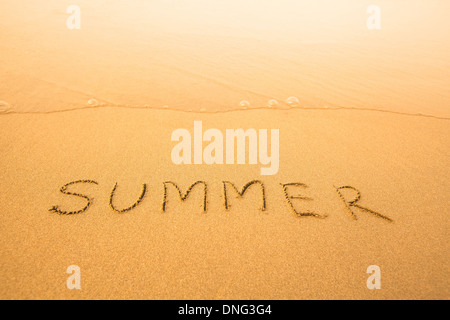 Sommer - Text geschrieben von Hand im Sand am Strand, mit einer sanften Welle Stockfoto